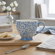 Blue and white patterned mug on a wooden table with cookies and a spoon.