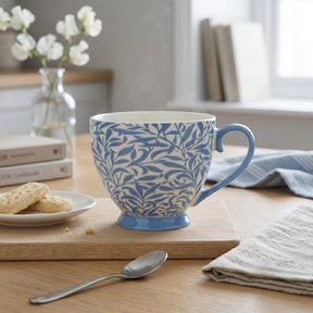 Blue and white patterned mug on a wooden table with cookies and a spoon.