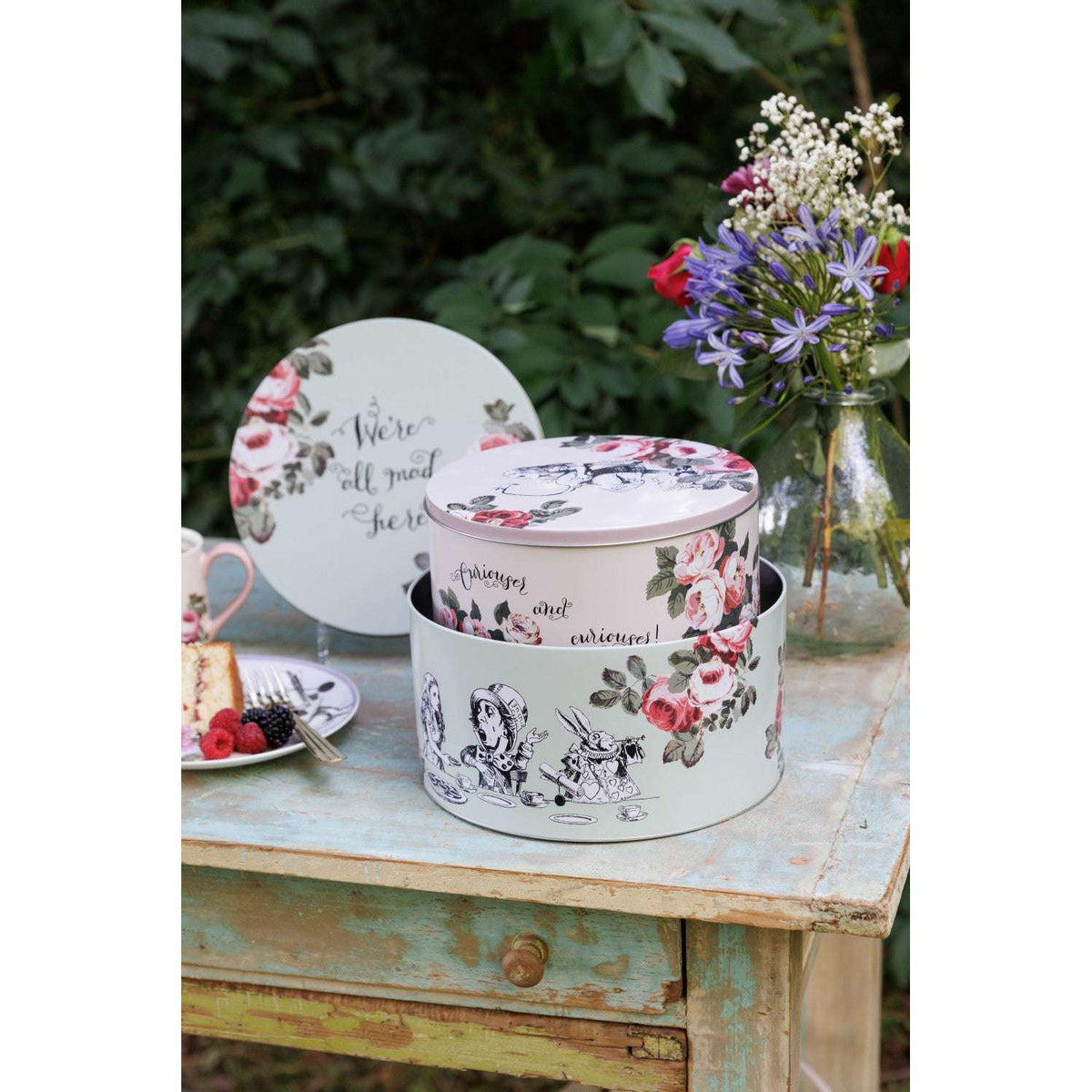 Mikasa Alice In Wonderland Cake Tins set against a backdrop of a tea party, showcasing their whimsical design.