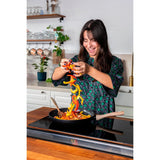 Image of a woman joyfully incorporating colourful peppers into the Pyrex Cook & Care recycled aluminium frying pan, perfect for vibrant meals.