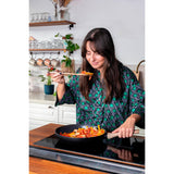 Close-up of a woman using chopsticks to lift colorful vegetables from the Pyrex Cook & Care recycled aluminium frying pan, showing healthy cooking in action.