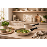 A beige non-stick frying pan and matching saucepan with black handles sat on a light wood kitchen counter.