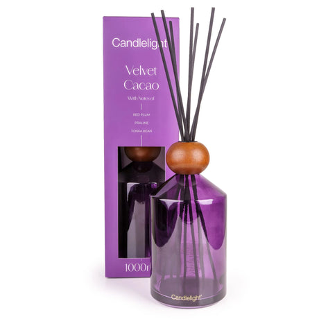 A purple glass reed diffuser bottle with a wooden sphere stopper and dark reeds, standing in front of its matching purple Candlelight 'Velvet Cacao' box on a white background.